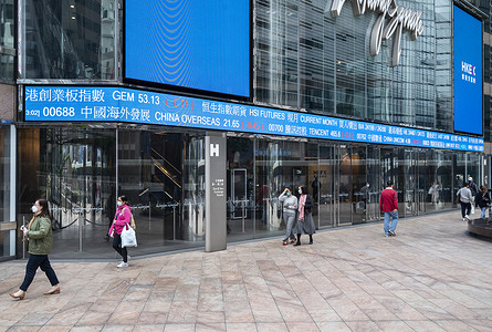 Pedestrians walk past a stock market display board showing the Hang Seng Index results in Hong Kong.