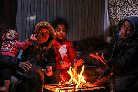 Palestinian children sit around a fire to keep themselves warm inside their house during a rainy and windy day on the outskirts of Khan Yunis refugee camp in the southern Gaza Strip.